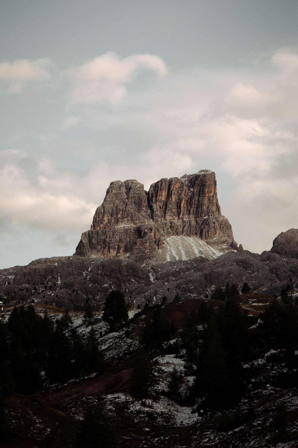 A blocky rock summit above dark forest with light snow on the ground